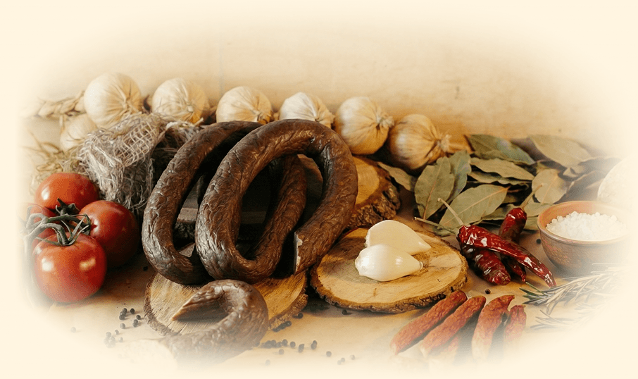 Zdjęcie przedstawiające ładnie zaprezentowaną kiełbase otoczoną świerzymi ziołami przyprawami i warzywami